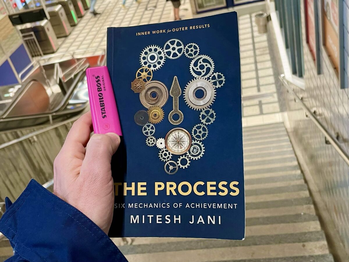 The Process by Mitesh Jani — book held with pink highlighter at train station